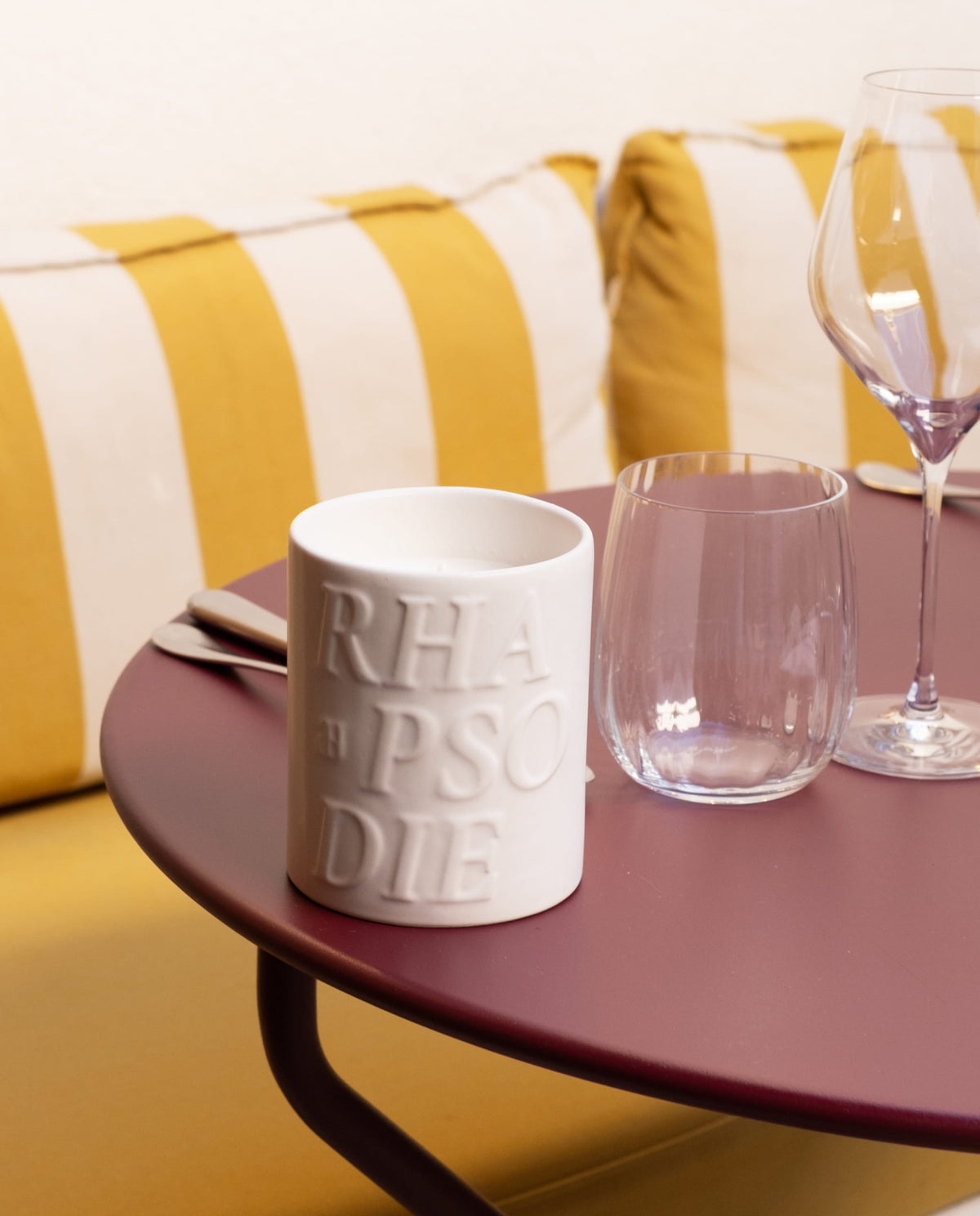Bougie Amara sur une table de bistrot bordeaux, devant une banquette rayée jaune