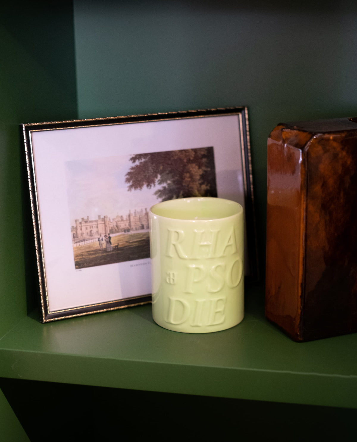 Bougie Capri sur une étagère verte, près d'un cadre et d'un vase en bois