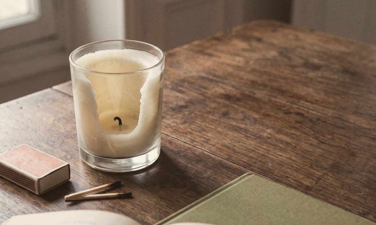 Bougie en verre dont la cire est restée contre la paroi, sur une table en bois