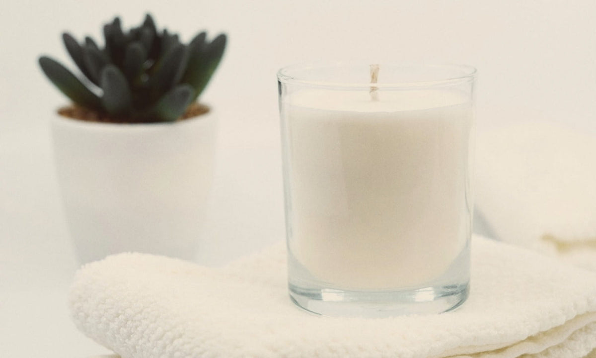 Bougie blanche dans un verre transparent, posée sur une serviette