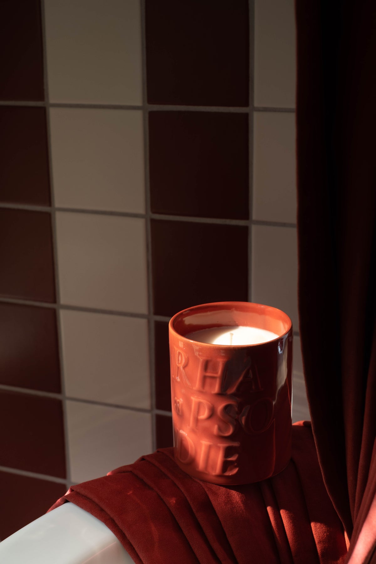 Bougie Véraison allumée au bord d'une baignoire, un drap rouge à côté