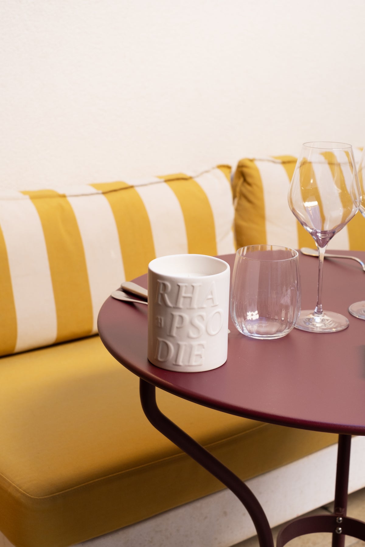 Bougie Amara sur une table de bistrot bordeaux, devant une banquette rayée jaune