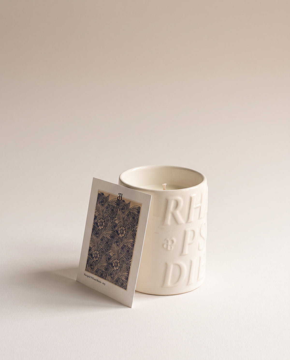 Bougie Amara dans sa céramique émaillée ivoire, avec le feuillet du papier peint Marigold de William Morris