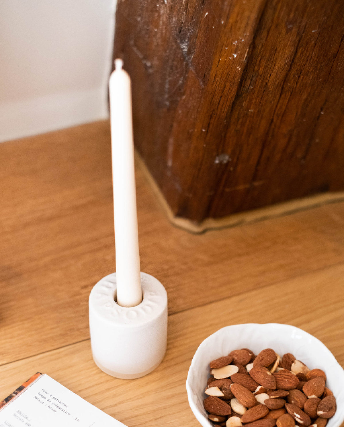 Bougeoir Amara et sa chandelle sur une table en bois, à côté d'un bol d'amandes