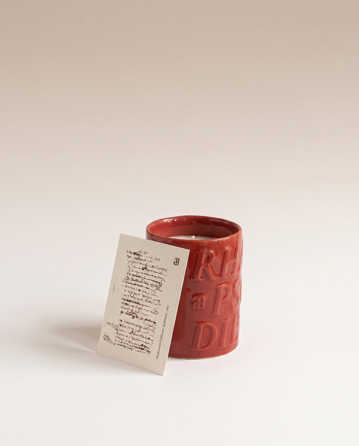 Bougie Véraison dans sa céramique émaillée rose orangé, avec le feuillet du poème « Vendémiaire »